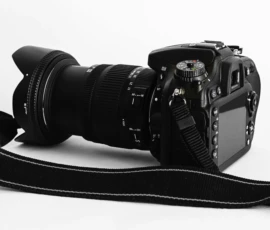Photo credit: PH Crisher Close-up of a DSLR camera with lens and strap on a white background.