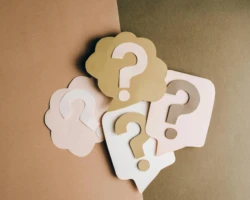 Photo credit: Leeloo the First Four paper cutouts of question marks in beige and white on a brown surface, symbolizing inquiry and curiosity.